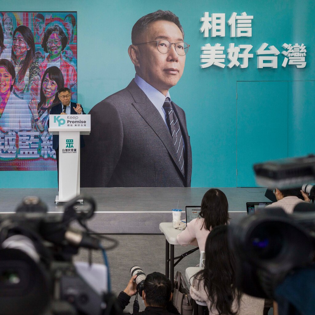 Ko Wen-je speaks at a podium with a large photo of himself on the wall behind him. 