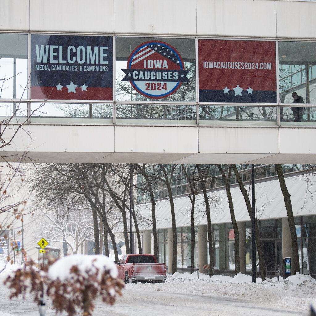 A snowy road and buildings in Iowa. Iowa Caucus signs hang in a pedestrian walkway between two buildings.