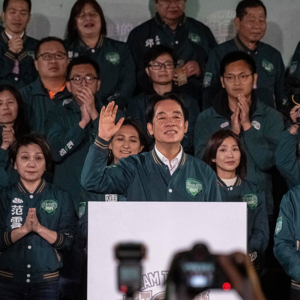 Mr. Lai stands at a lectern, one hand raised. He and a crowd of people behind him are all wearing matching green jackets.