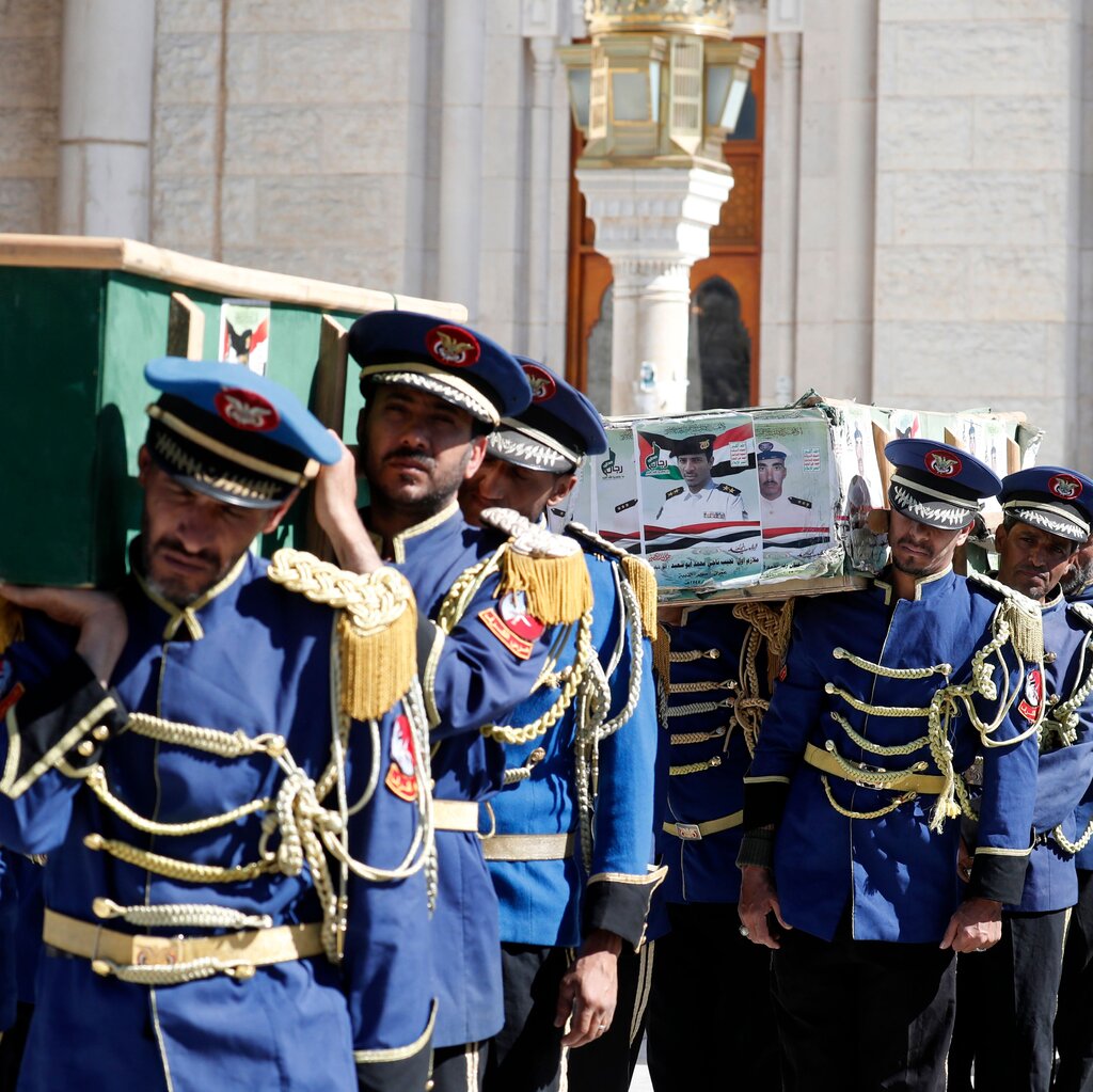 An honor guard in blue uniforms with gold tassels carrying coffins on a street.