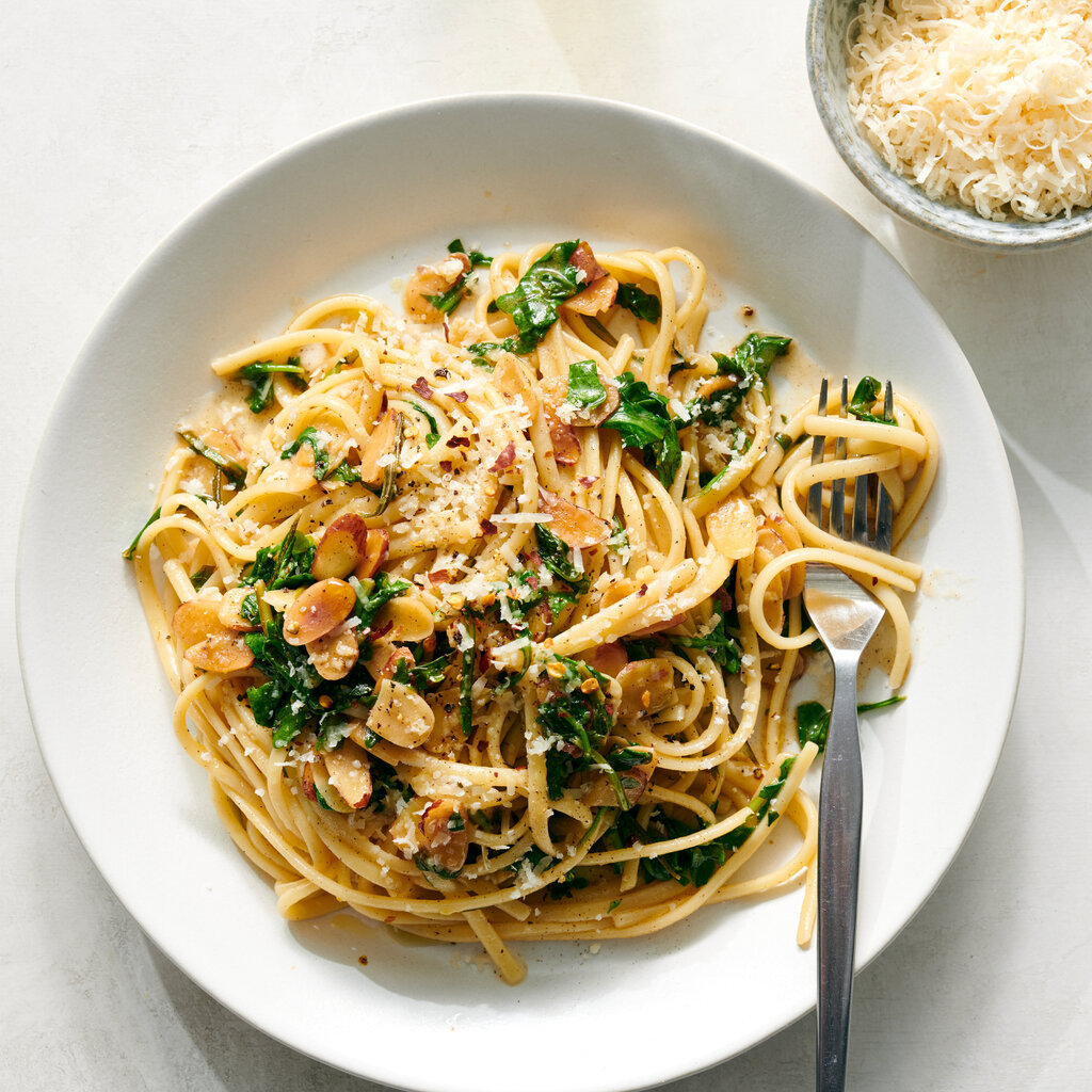 A plate of spaghetti, with arugula and topped with almonds and cheese. 