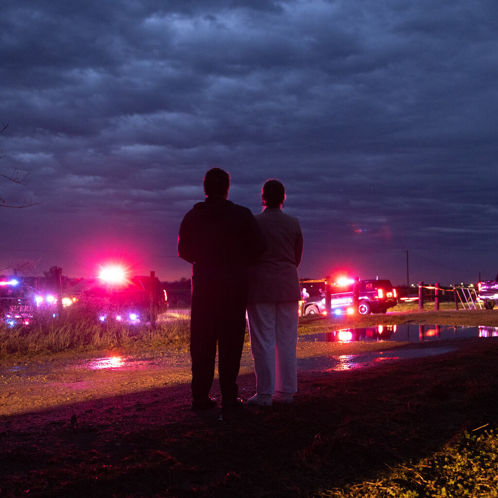 People stand in the light of police cars outside a prison. 