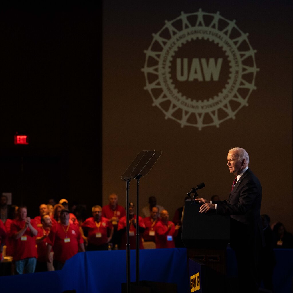 President Biden speaking at a podium with the UAW logo behind him.