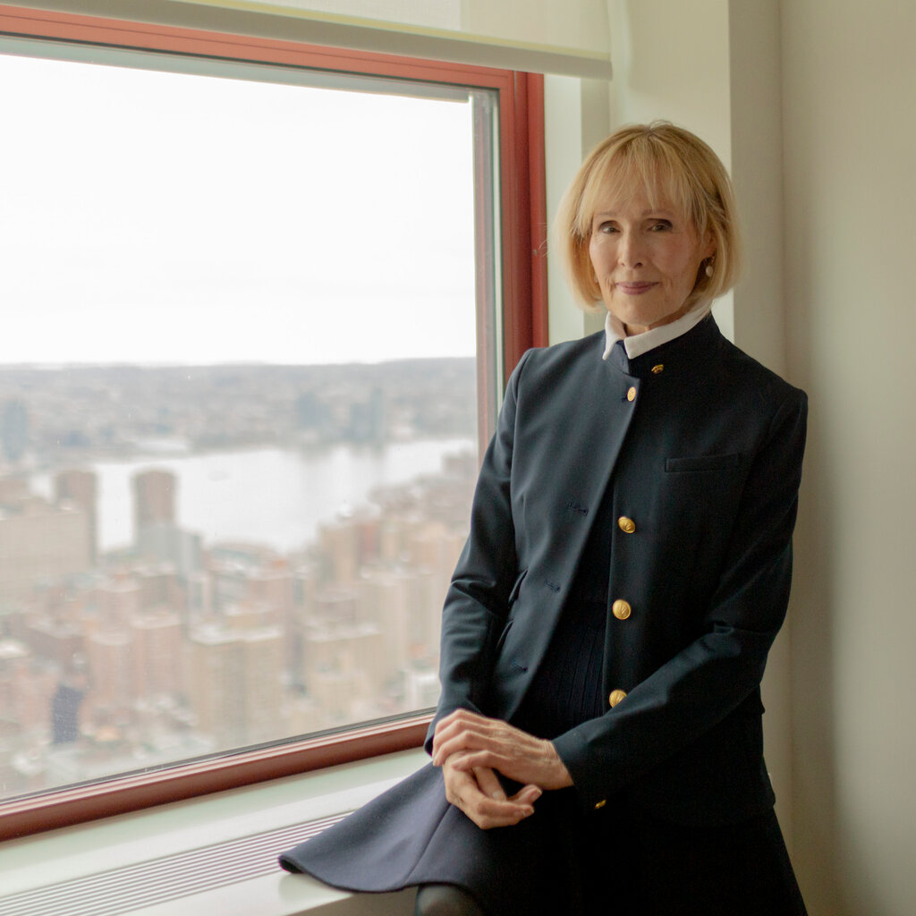 E. Jean Carroll in a high-collared dress next to a window overlooking the Hudson River.