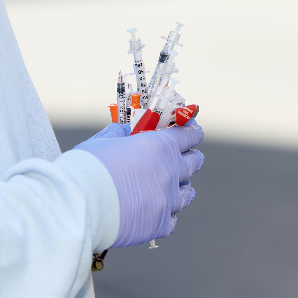 A person wearing latex gloves holding used syringes.
