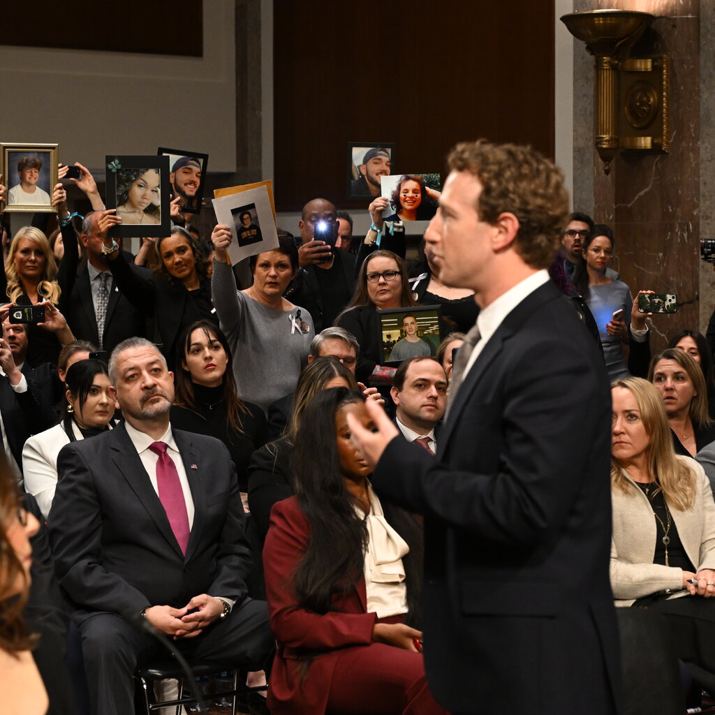 Mark Zuckerberg standing in front of people holding up images of children. 