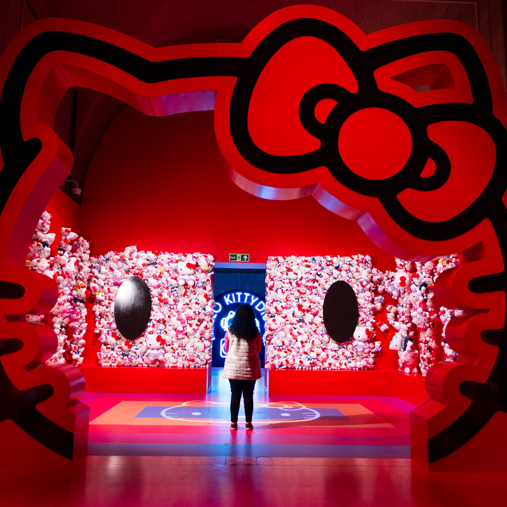 A woman stands in front of a large red installation shaped like Hello Kitty’s head.