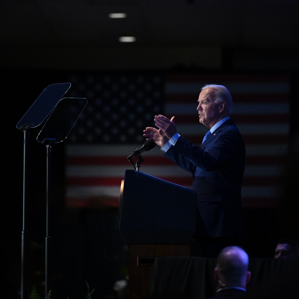 President Joe Biden speaks at a podium with his arms raised. 