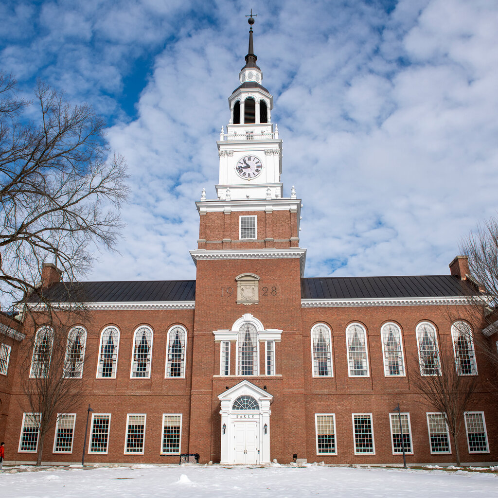 The exterior of a brick building with a large clock tower. Snow covers the ground in front of the building. 