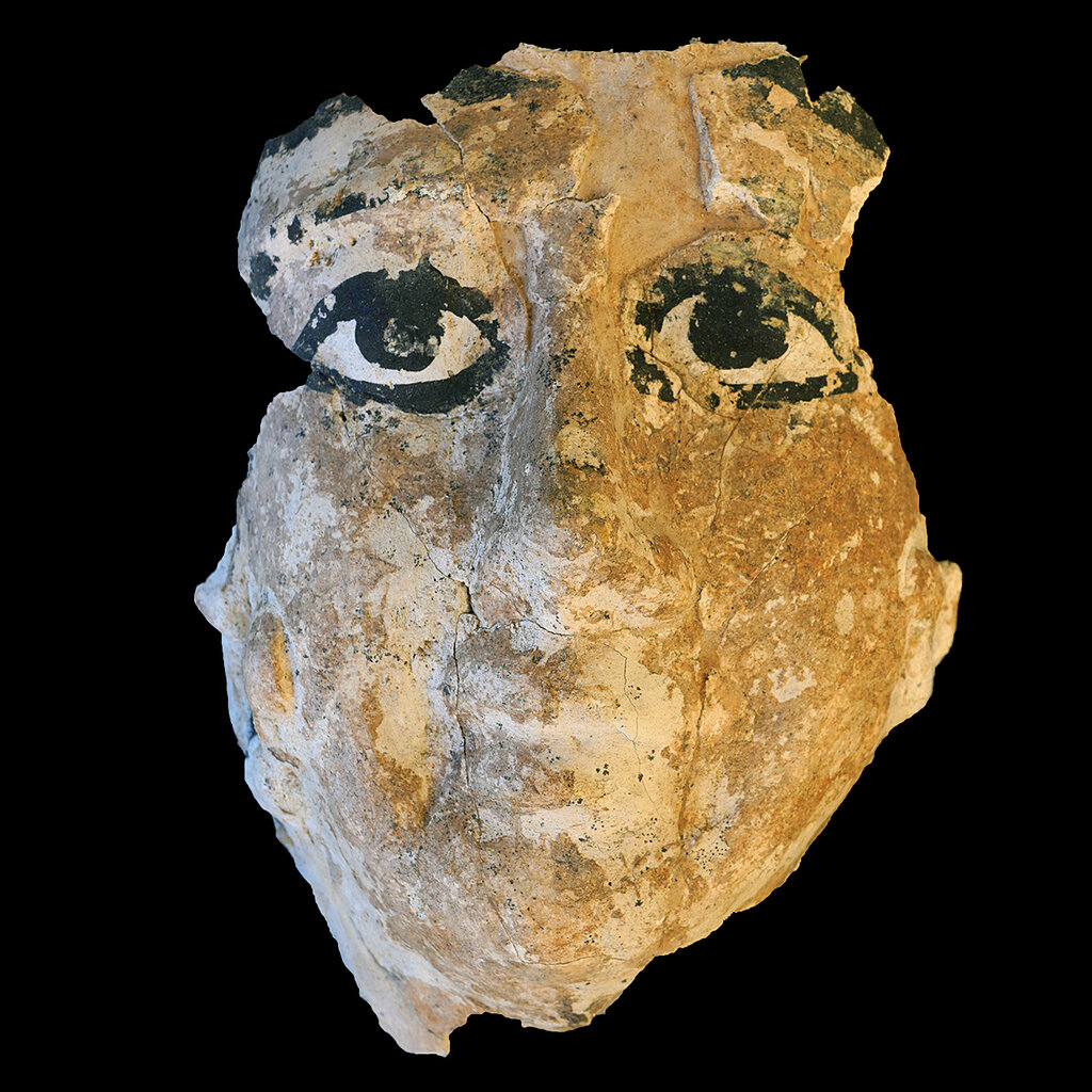 A fractured clay mask with painted eyes.