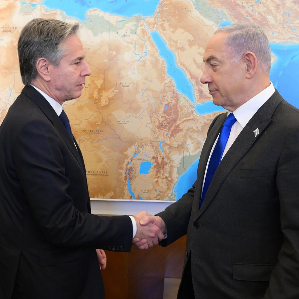 The American secretary of state shaking hands with the leader of Israel in front of a large map.