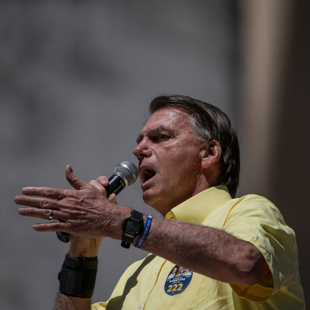 Jair Bolsonaro in a yellow shirt speaking into a mic.
