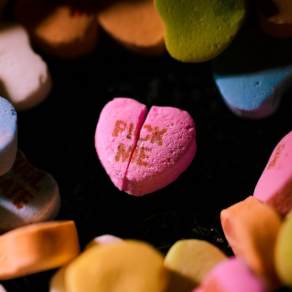A close-up of a pink candy heart that reads "Pick Me" and is split in half.