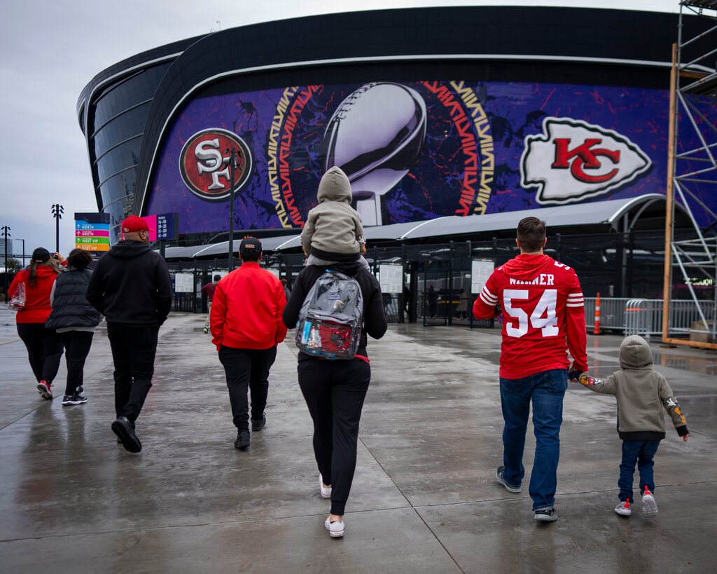 Football fans walk toward a stadium with Super Bowl branding.
