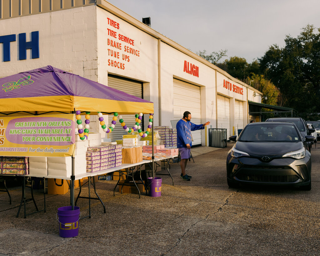 Cars line up next to the side of a garage and approach a large table containing boxes. 