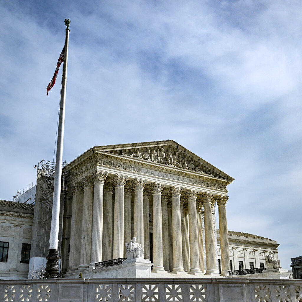 The exterior of the U.S. Supreme Court building. A large flag pole sits in the foreground.