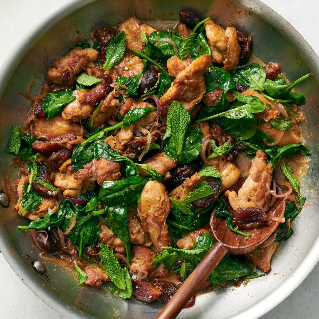 A stainless steel skillet holds gingery chicken with dried apricots, spinach and a showering of mint leaves.