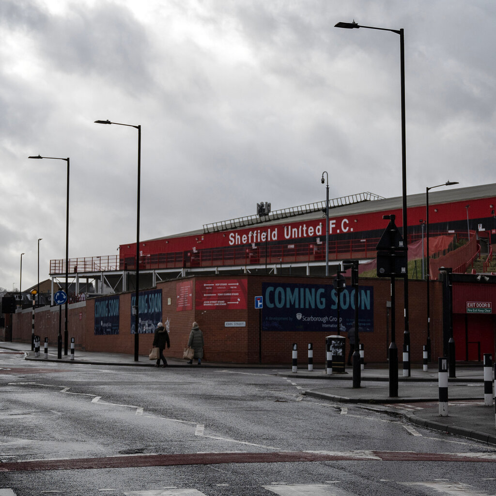 A view from the street of Bramall Lane, the stadium that bears the name of its occupant, Sheffield United F.C., in white lettering on its red wall.