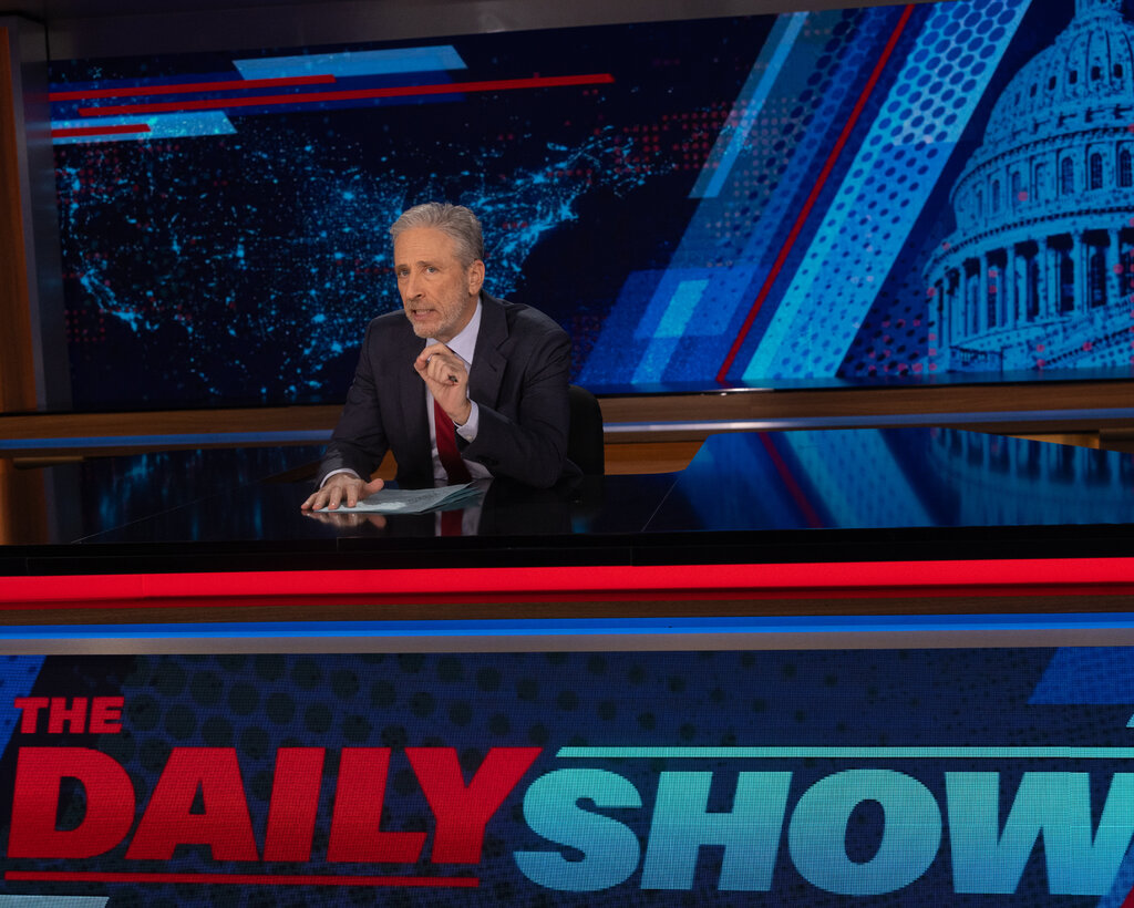 Jon Stewart at the “Daily Show” desk, gesturing to emphasize a point