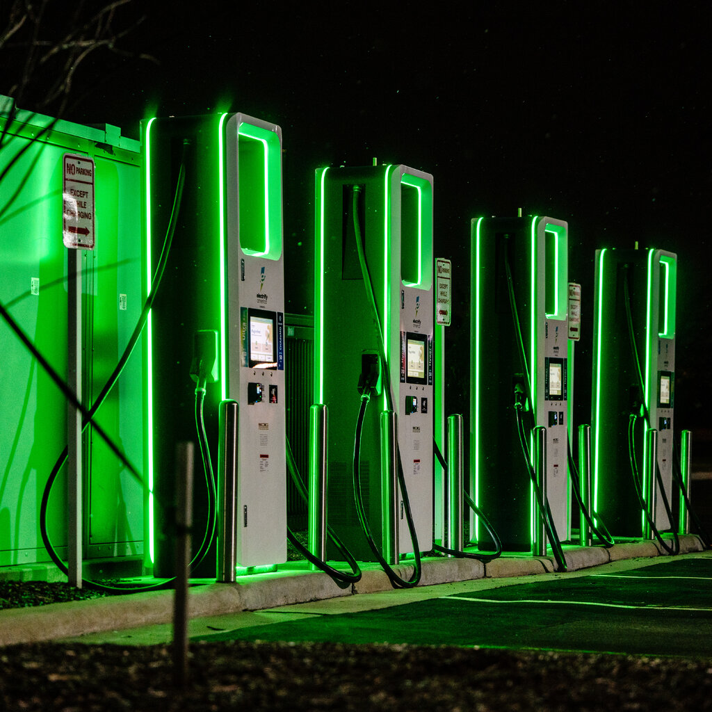 Green neon lighting outlines a row of four vehicle charging stations at night. 