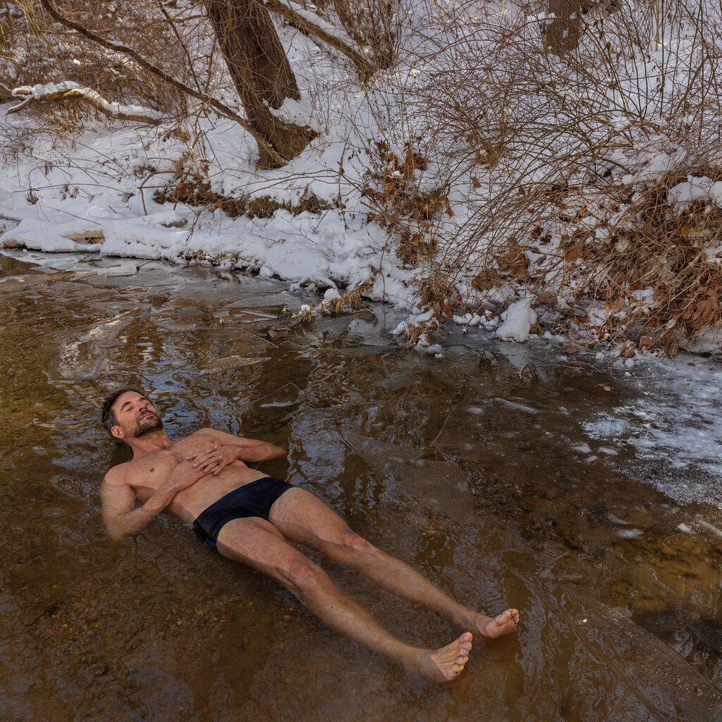 Bradley Cooper laying in a hot spring, surrounded by snow.