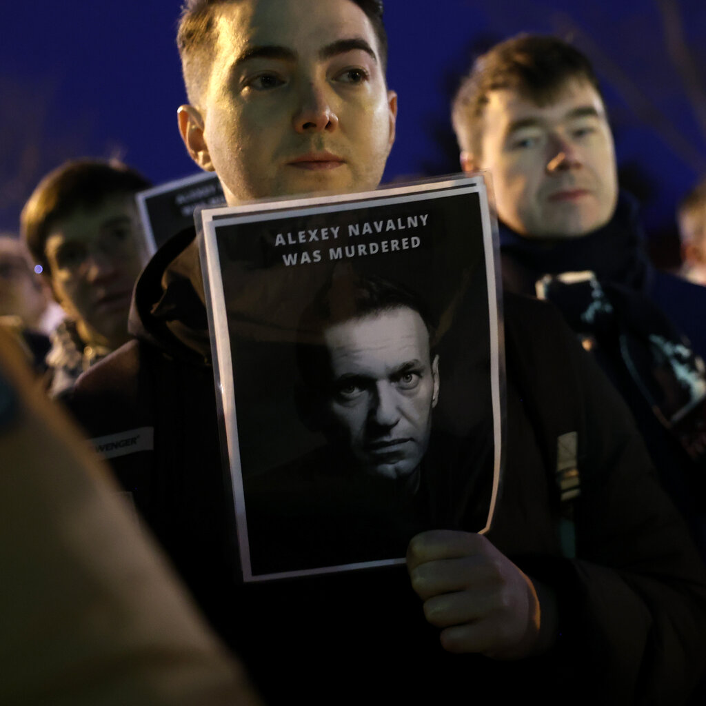 A man in a crowd holds a sign with a picture of Aleksei A. Navalny and the text “Alexey Navalny Was Murdered.”