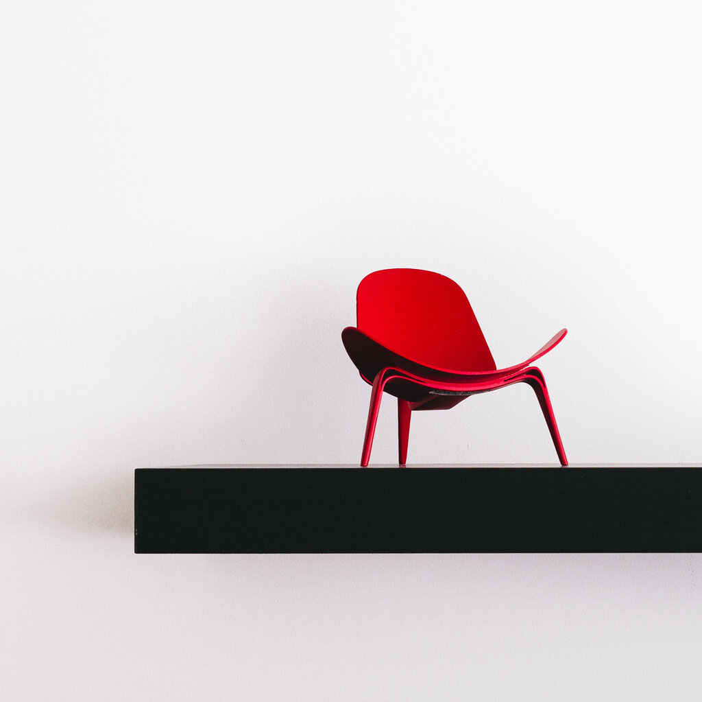 A red chair on a black platform in a white room.