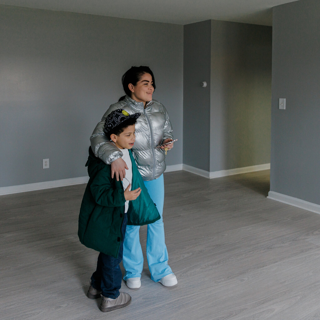A woman and a child stands in an empty gray room. 