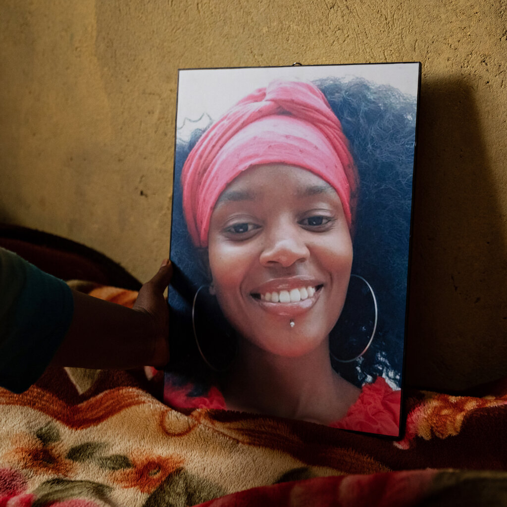 A hand holding a photograph of a smiling young woman in a pink headwrap and hoop earrings. 