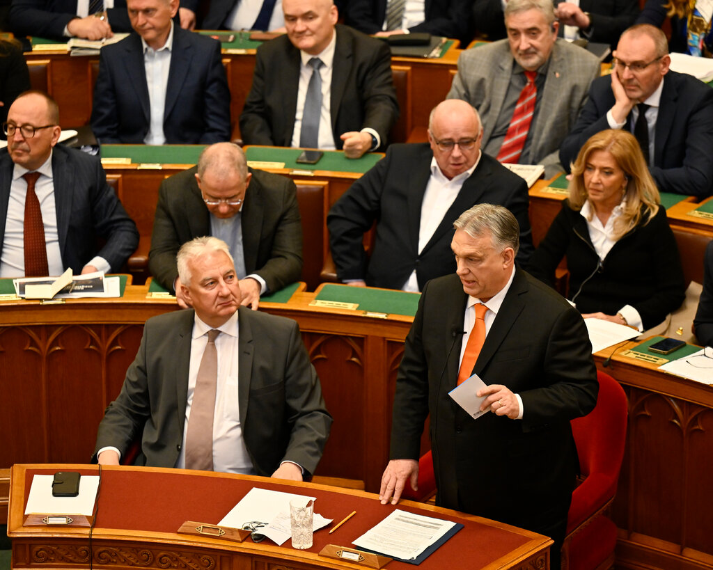 Viktor Orban speaking in Parliament, surrounded by lawmakers.