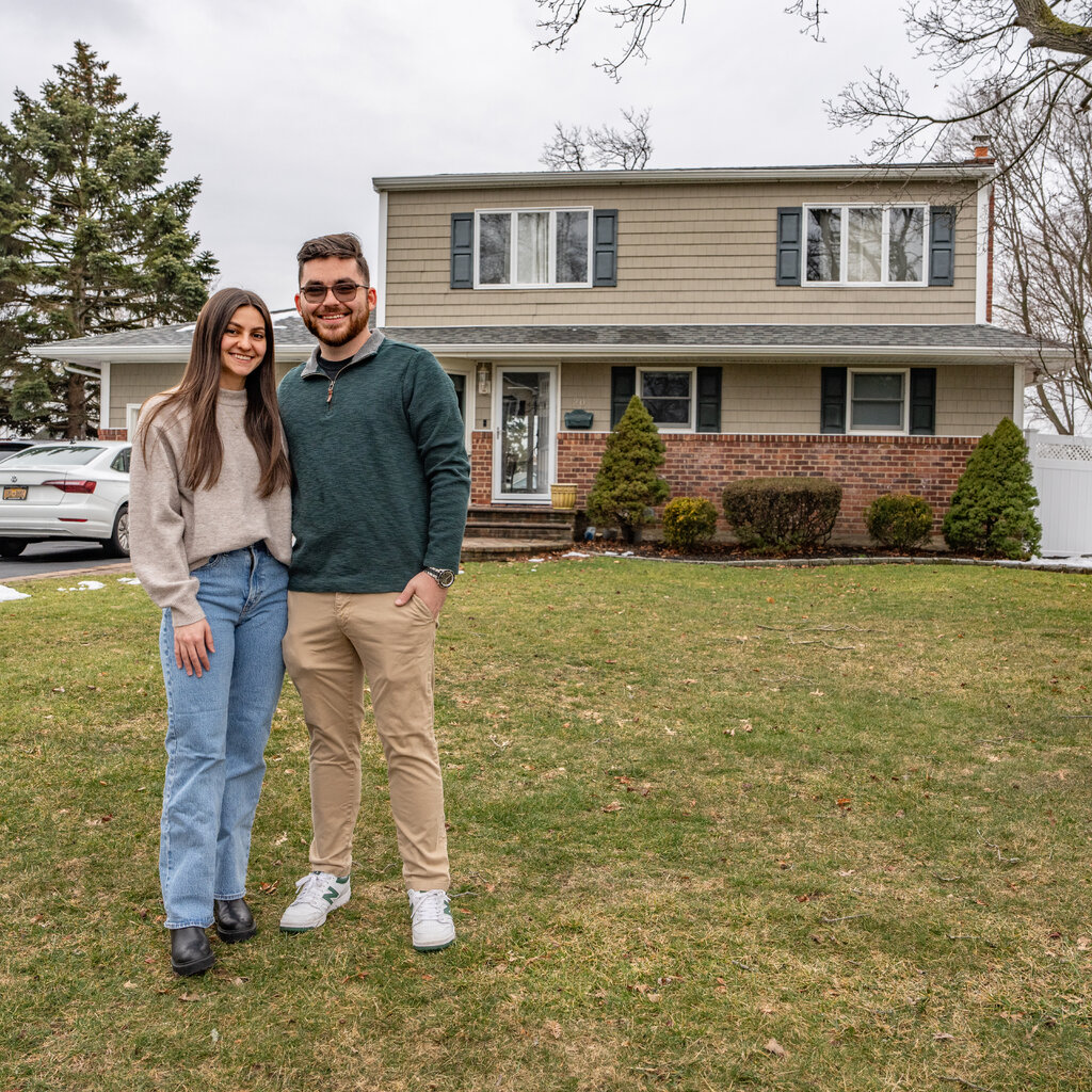 A couple stand in front of a house, her childhood home, which they are buying.
