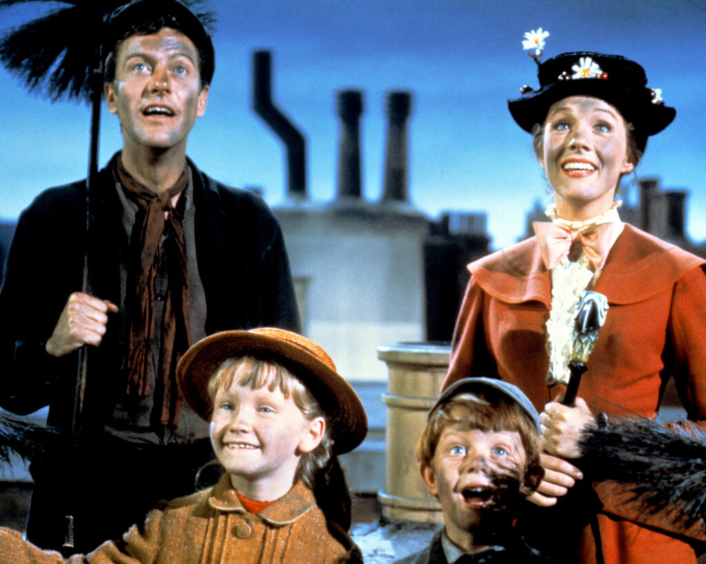 In an image from “Mary Poppins,” Dick Van Dyke is dressed as a chimney sweep and Julie Andrews is wearing a red dress. They are standing with two children.
