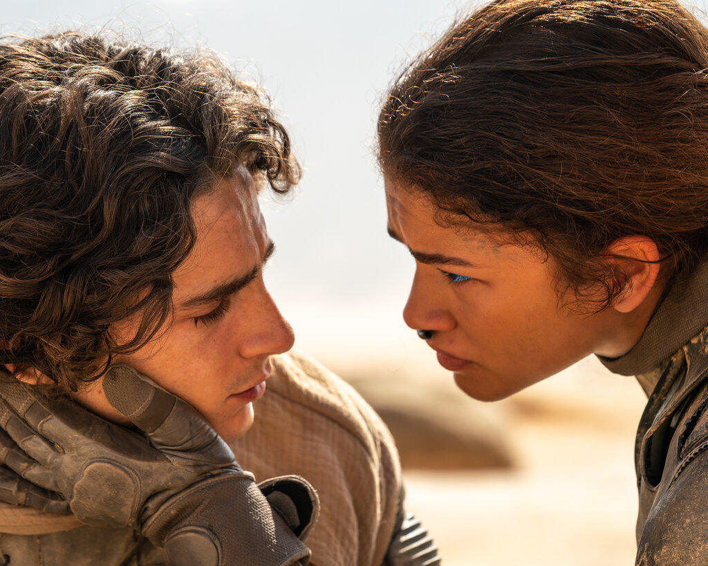 In a sci-fi-looking scene set in the desert, Zendaya holds a gloved hand to Timothée Chalamet’s cheek.