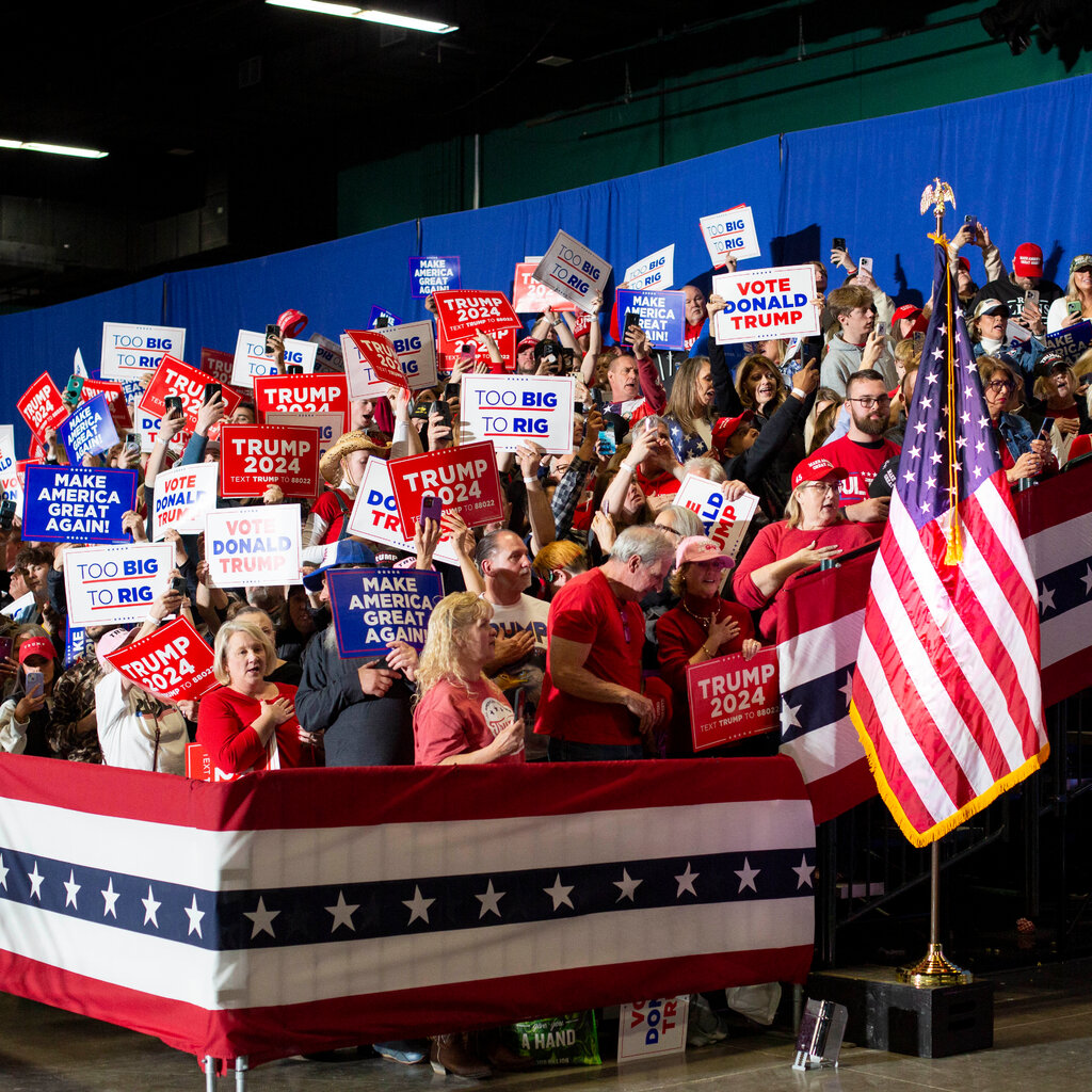 Trump supporters at an event, holding up campaign signs. 