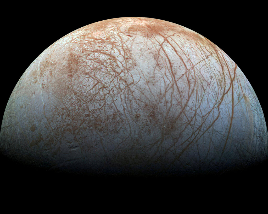 Half of the world Europa, with brownish streaks on its surface, emerging from shadow.