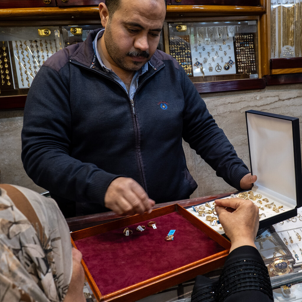 A man shows jewelry to two woman in a shop.