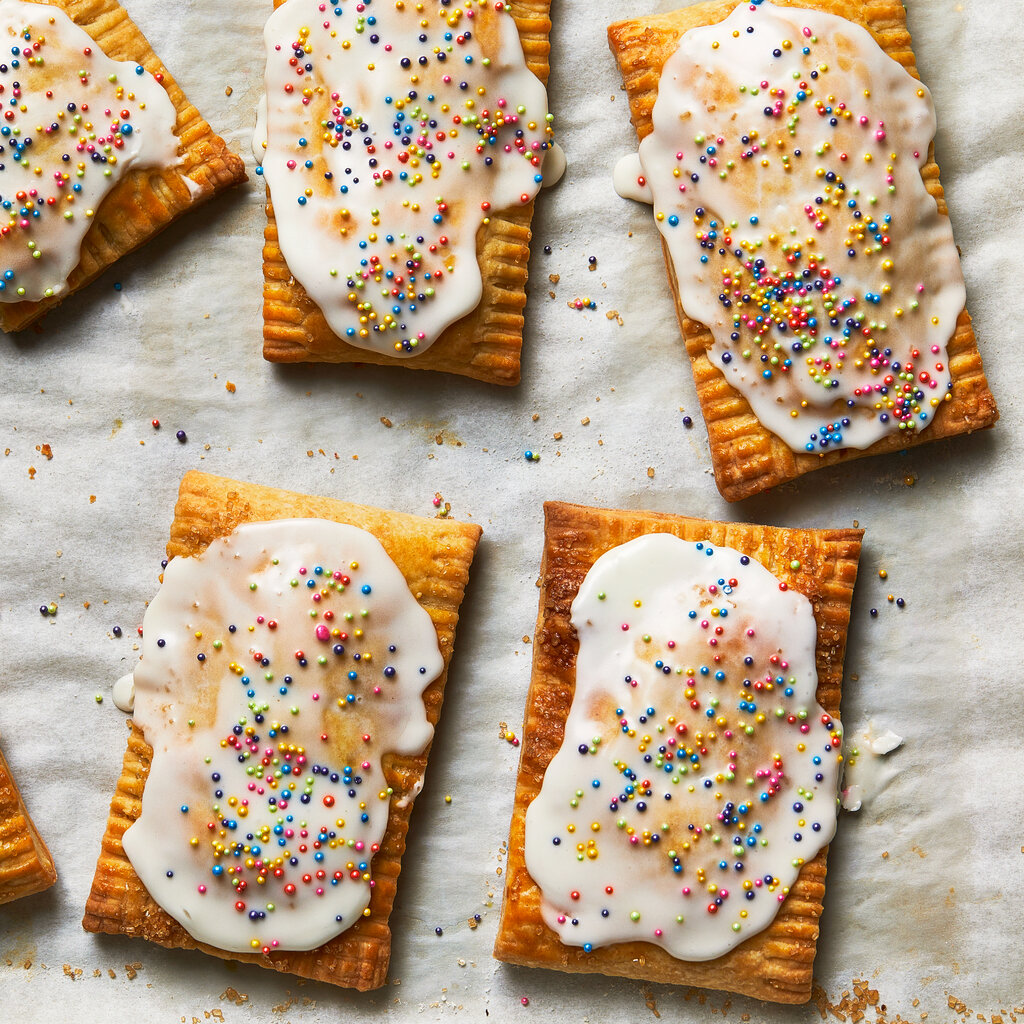 A top-down view of five Pop-Tarts with white frosting and multicolor toppings.