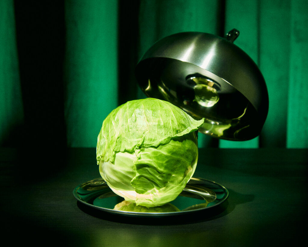 A head of cabbage sits on a silver platter against a green background. 