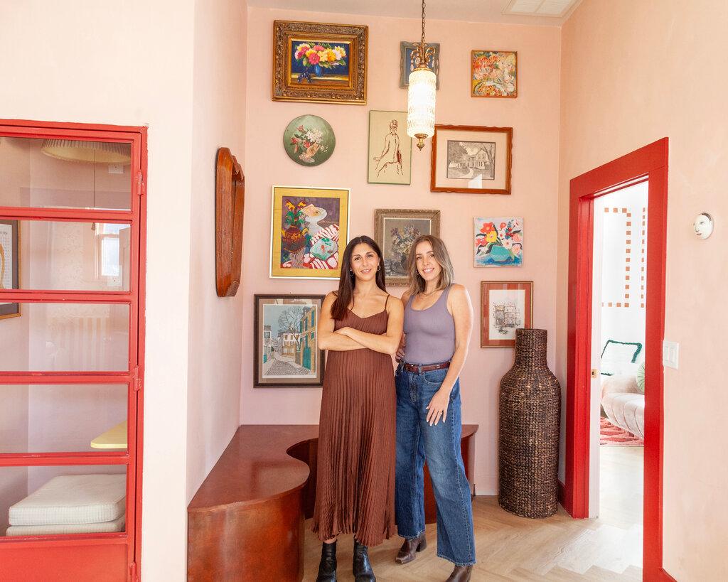 Two women stand beside each other in a home decorated with art.
