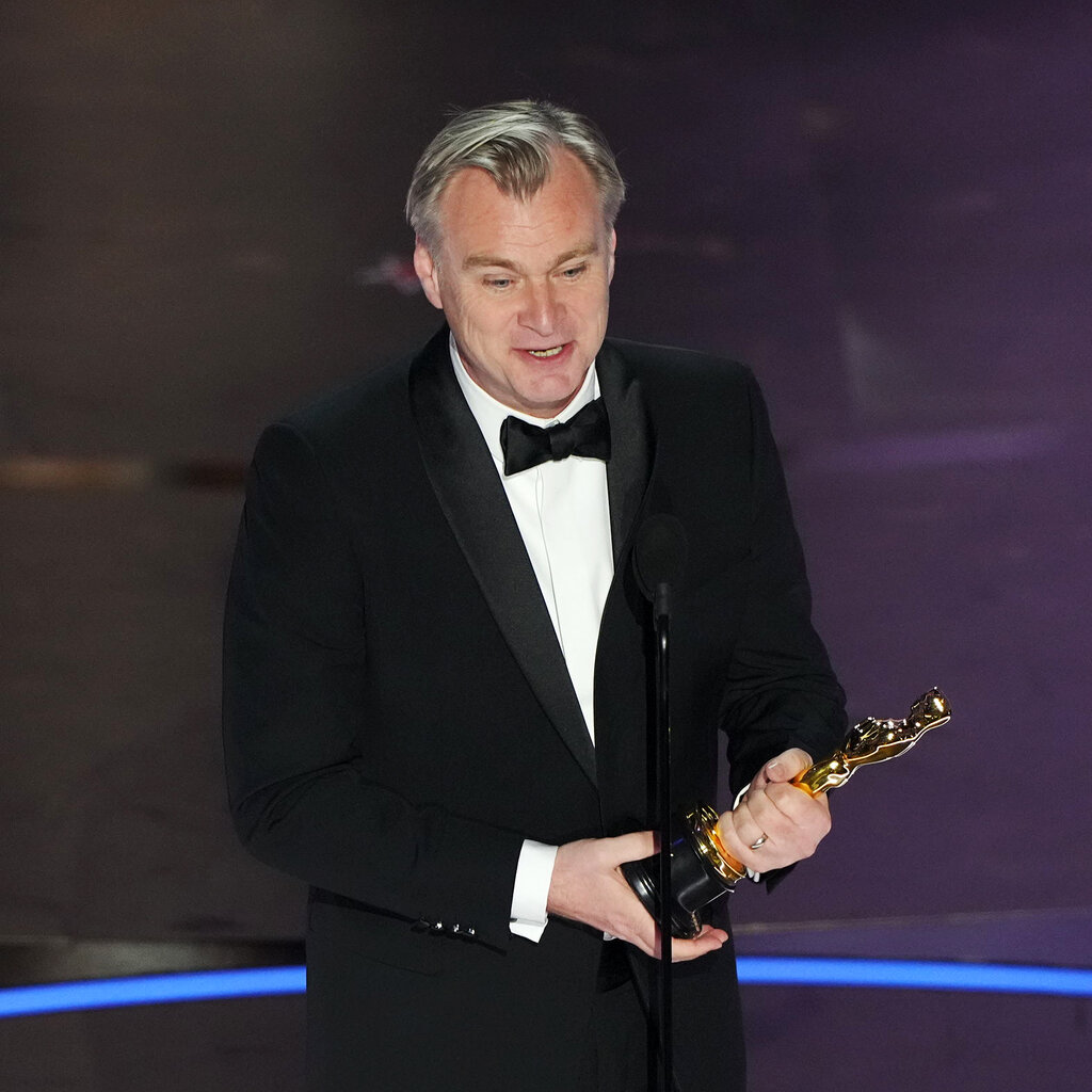 Christopher Nolan onstage holding an Oscar trophy.  