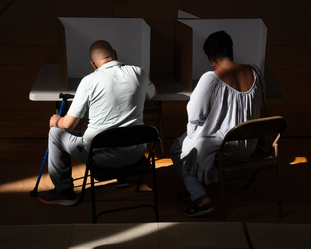 Two people sit at voting booths.