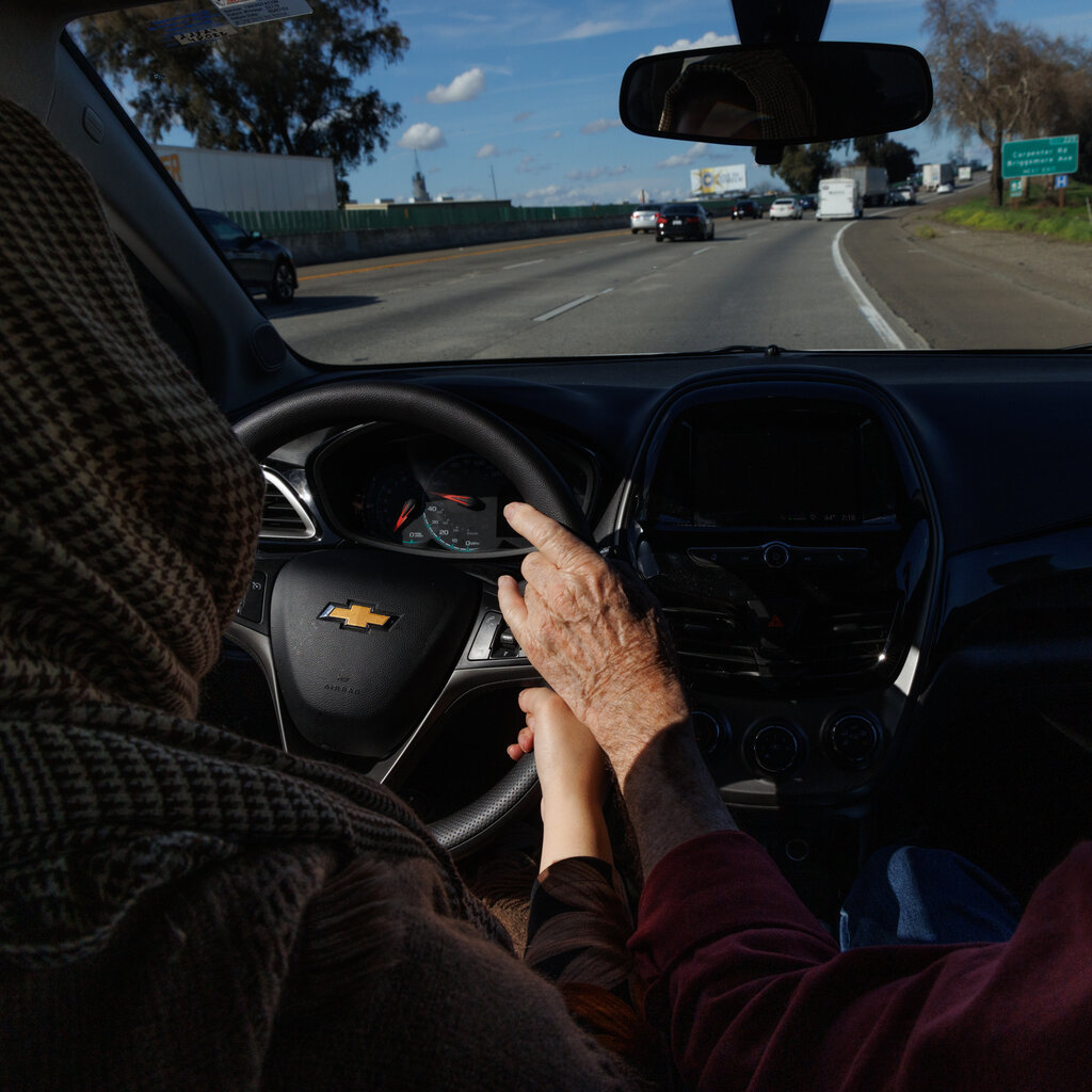 A view of a man’s hand helping guide the steering wheel during a driving lesson.