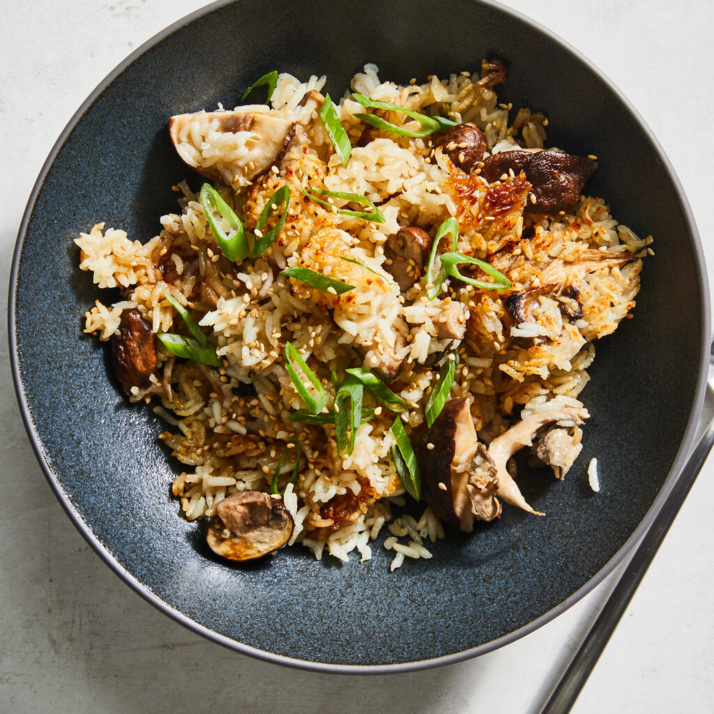 A dark blue ceramic bowl holds crispy one-pot mushroom and ginger rice scattered with scallions.