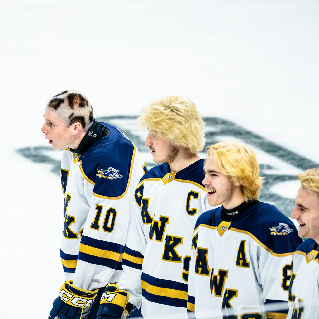 In a line of hockey players with bleached blond hair, one is leaning forward with his hair cut very short and dyed to look like a leopard’s spots.
