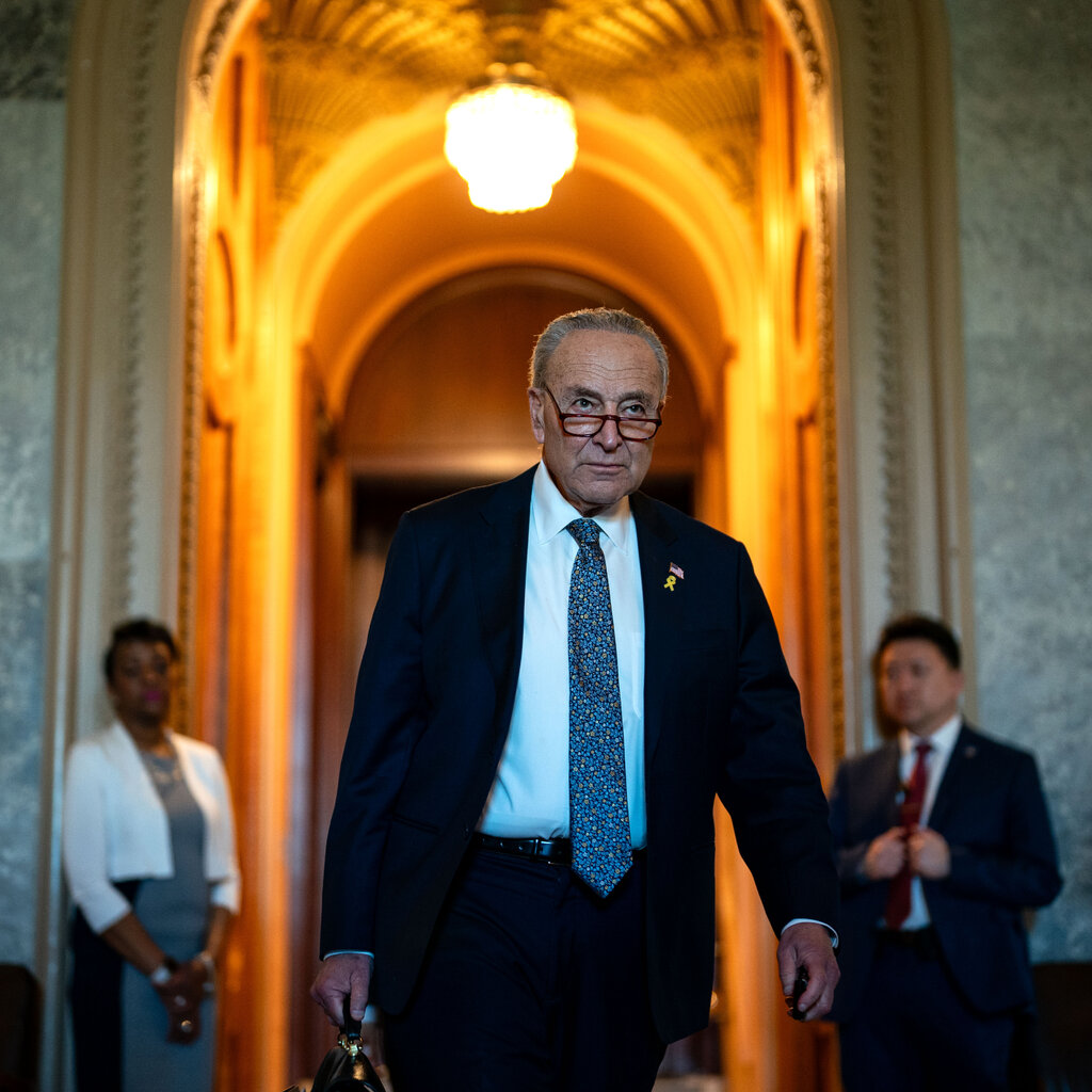 Chuck Schumer, in a dark suit and multicolor tie, walks through the Capitol. 