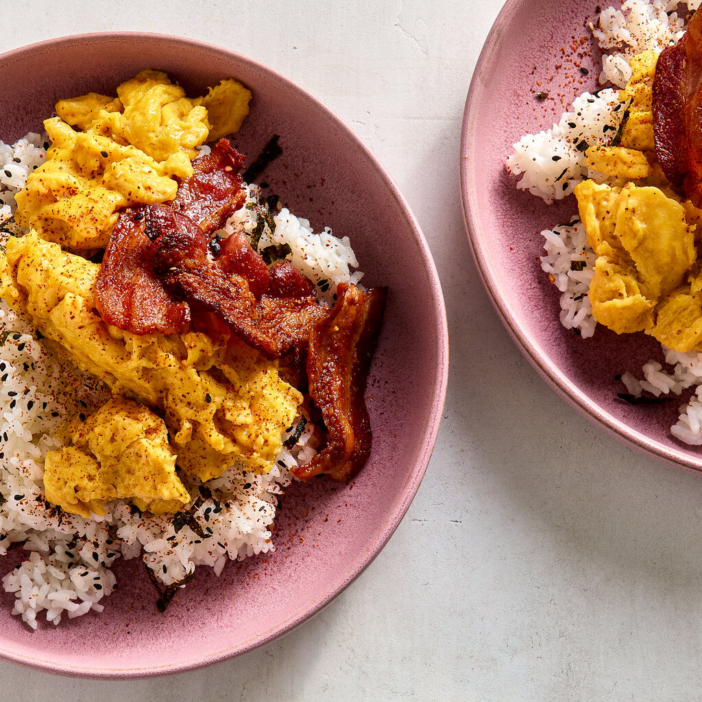 An overhead image of two pink bowls filled with rice that’s been topped with eggs and bacon.