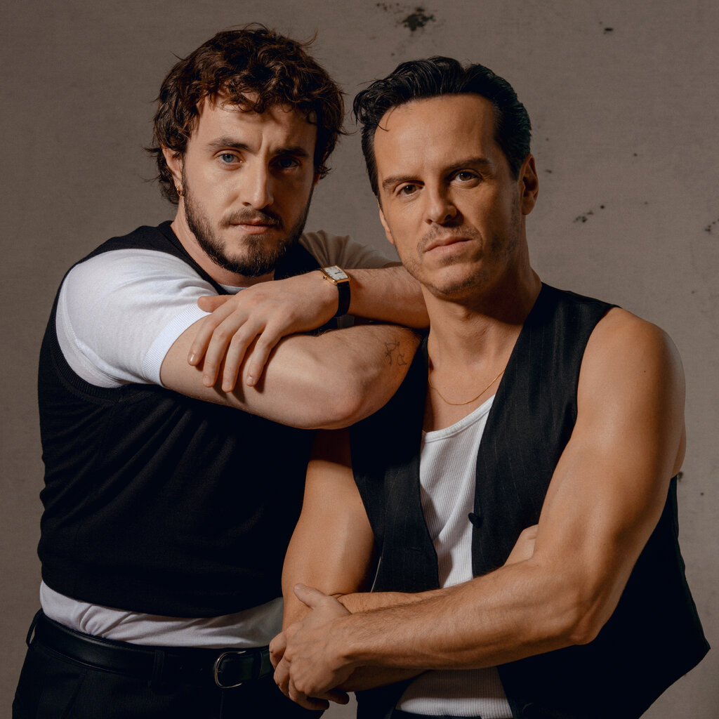 Paul Mescal, left, with messy hair and a beard, posing with his arms on the shoulder of Andrew Scott, who has stubble and slick brown hair. Mr. Mescal is wearing a cropped black vest over a white T-shirt and Mr. Scott is wearing a white tank top beneath a black vest that reveals his bare arms. 