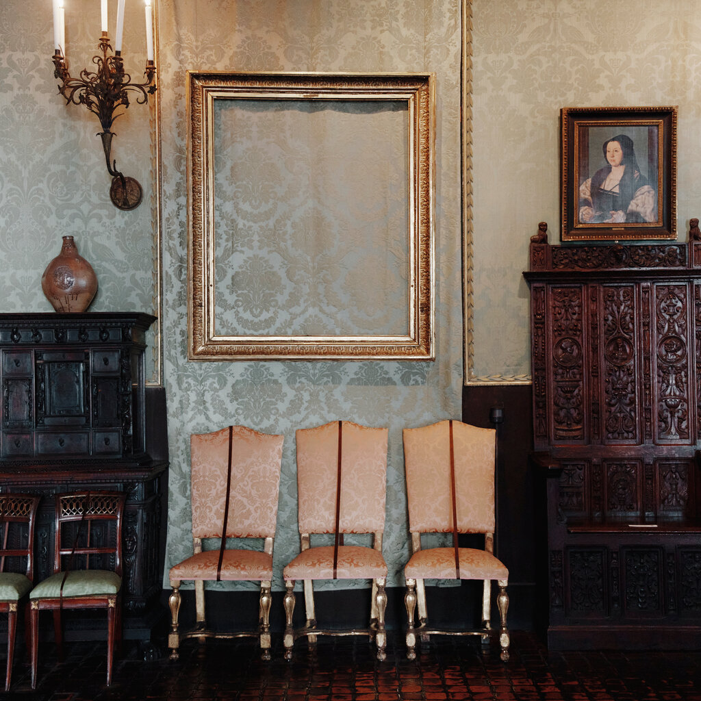 An empty frame hangs above three champagne colored chairs. 