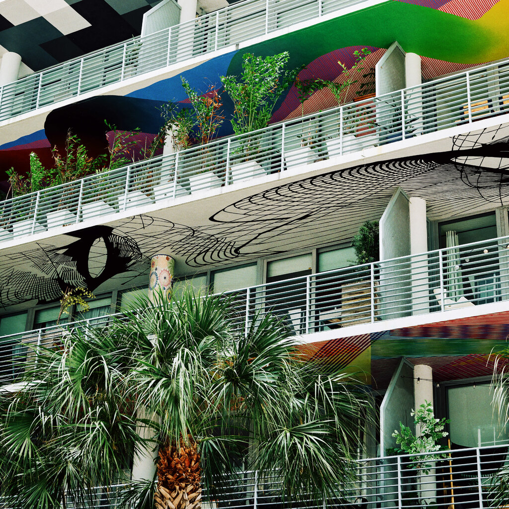 The facade of a multistory building with open balconies covered in colorful murals and plants.