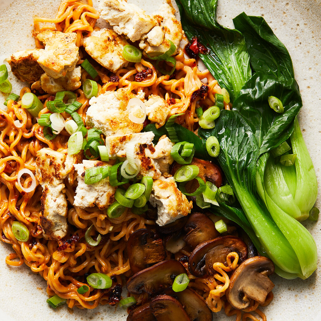 A white ceramic bowl holds a tangle of spicy tofu and mushroom mazemen with green baby bok choy.